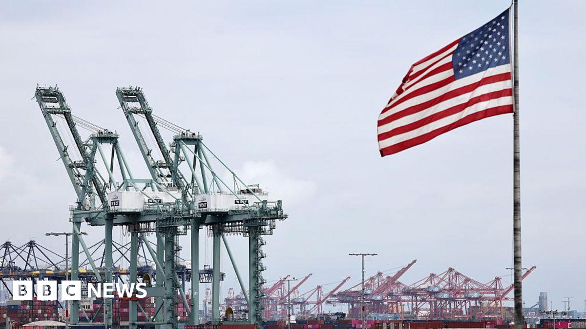 An American flag flies in front of shipping containers and cranes at the Port of Los Angeles on 26 September, 2025.