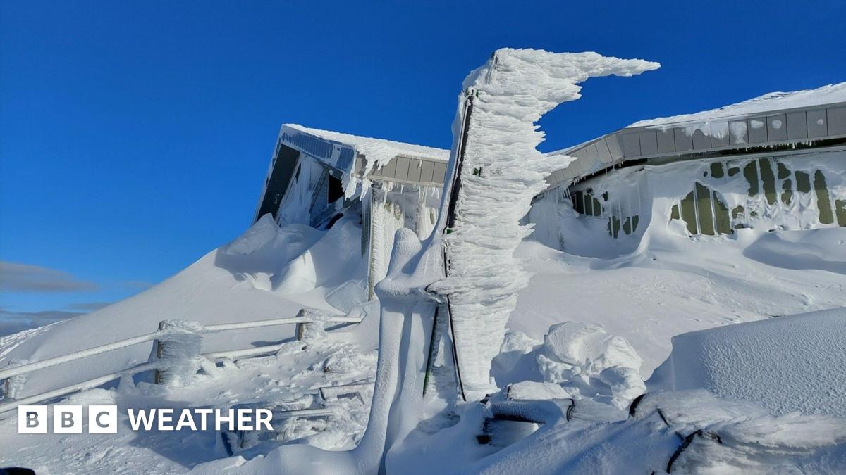 Bright blue skies are the back drop to a building with snow up the sides and on the ground and fence all around.