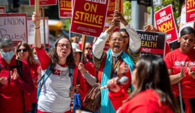 Hundreds of protestors in red T-shirts hold red and yellow picket signs outside of UCSF Benioff Children's Hospital Oakland.