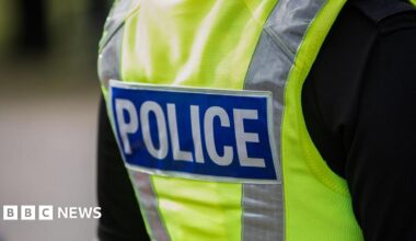The back of a police officer's jacket. It is yellow and has the word 'police' written on it in all capital letters.