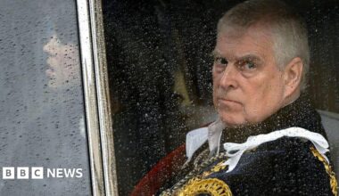 Andrew Mountbatten-Windsor seen through a carriage window - he is wearing ceremonial uniform. His daughter Eugenie can just be seen sitting alongside him