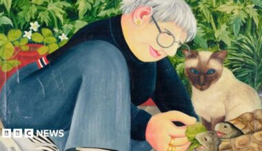 Artist Jo Beer is pictured in front of a self-portrait on the wall behind her.