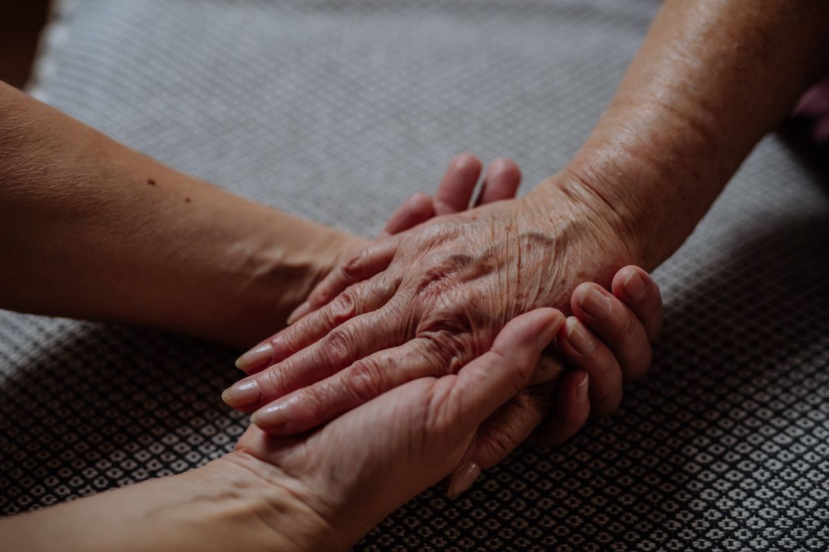 Hands of a senior woman and her daughter holding each other's hands together.