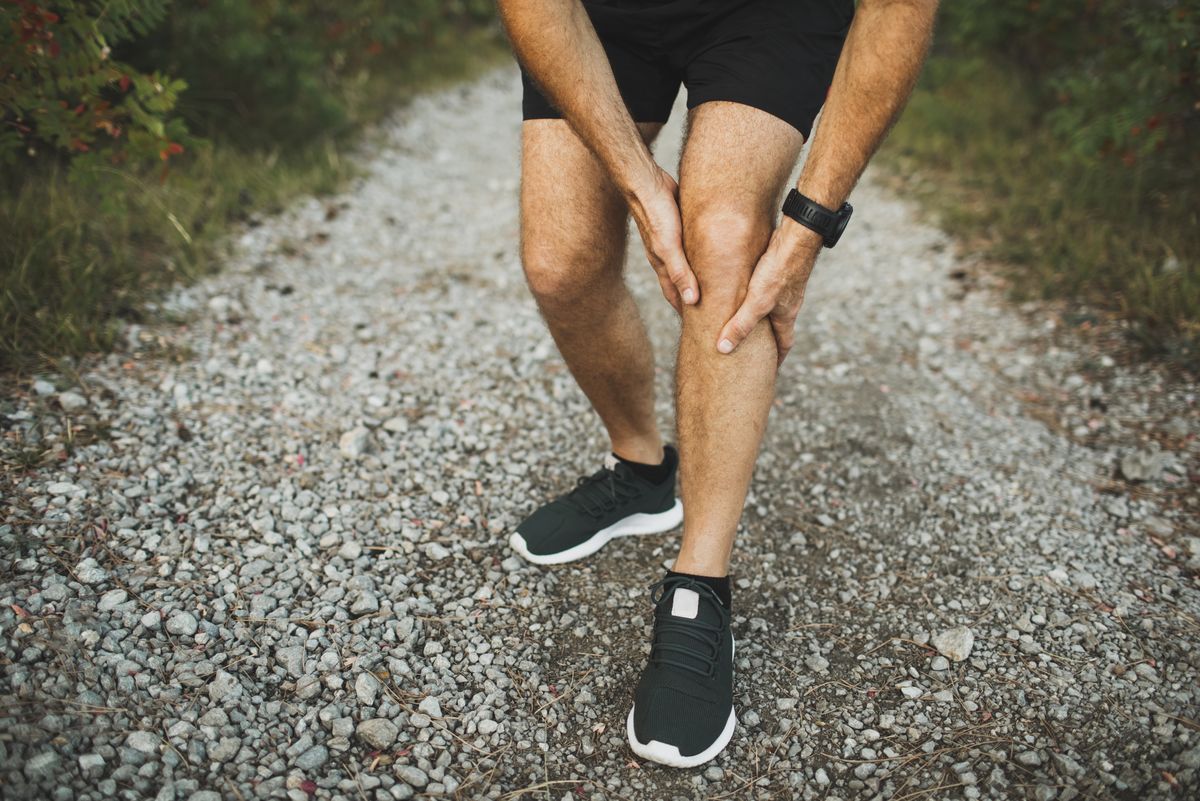 Knee injury on running outdoors. Man holding knee by hands close-up and suffering with pain. Sprain ligament or meniscus problem. Jogging and health problem. Accident and first aid. Inflammation of knee joint of runner athlete.