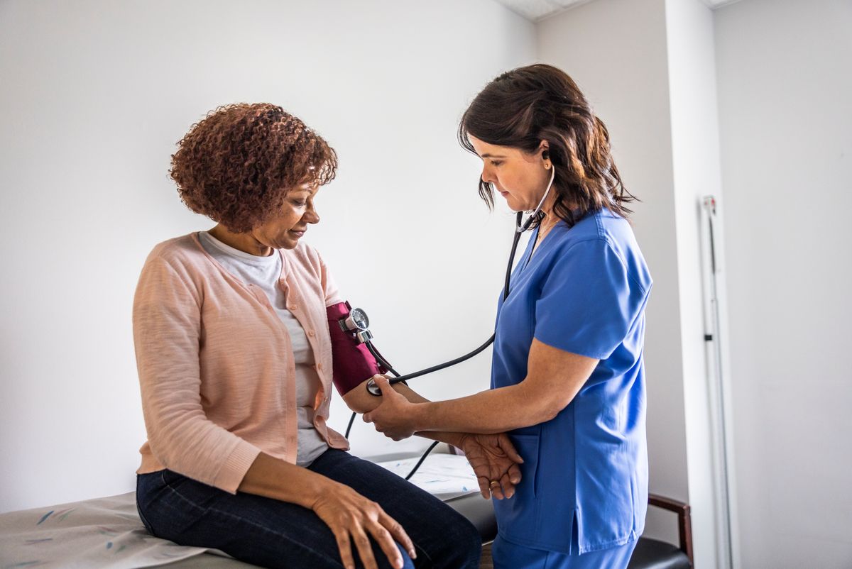 Nurse checking senior woman's blood pressure in exam room