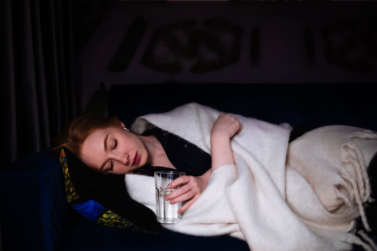 A woman rests on a sofa with a blanket, conveying a sense of peaceful tiredness. Her relaxed posture and calm expression, paired with soft lighting, capture a moment of serenity and quietude.