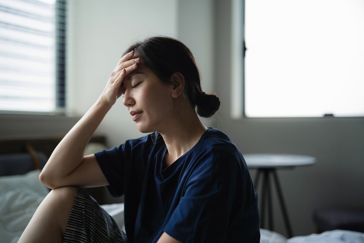 Young Asian woman with eyes closed resting on bed feeling headache. Exhausted woman with her hand on head not feeling well. Woman in pain. Concepts of mental health issues, wellbeing and illness