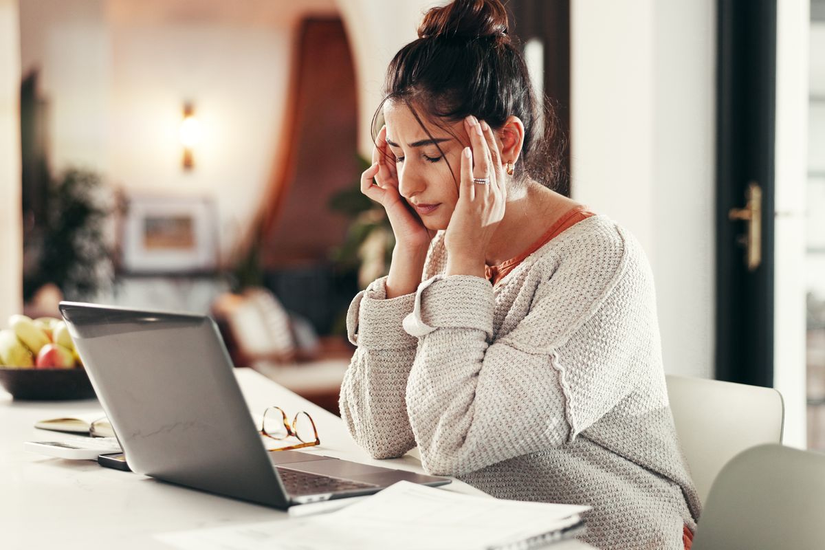 Woman looks stressed as she holds hands to head while working on laptop