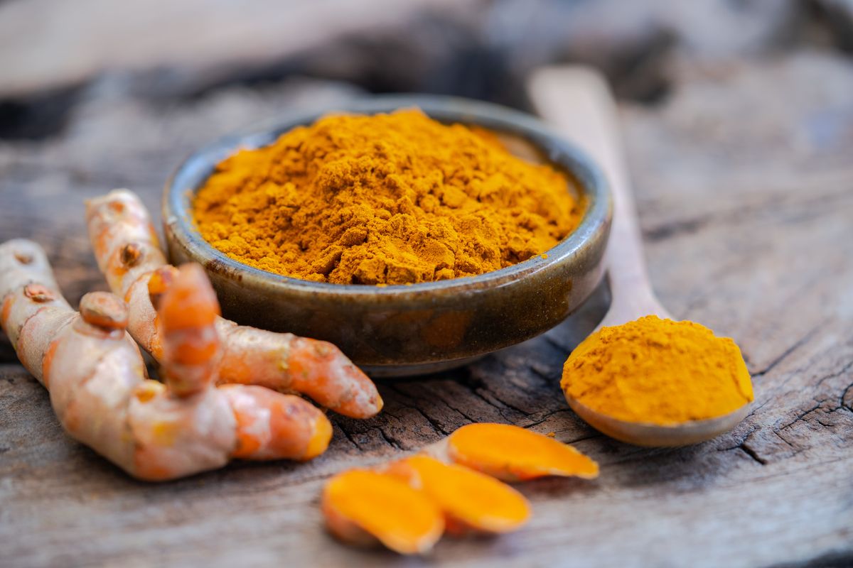Turmeric powder and fresh turmeric in wood bowls on wooden table.