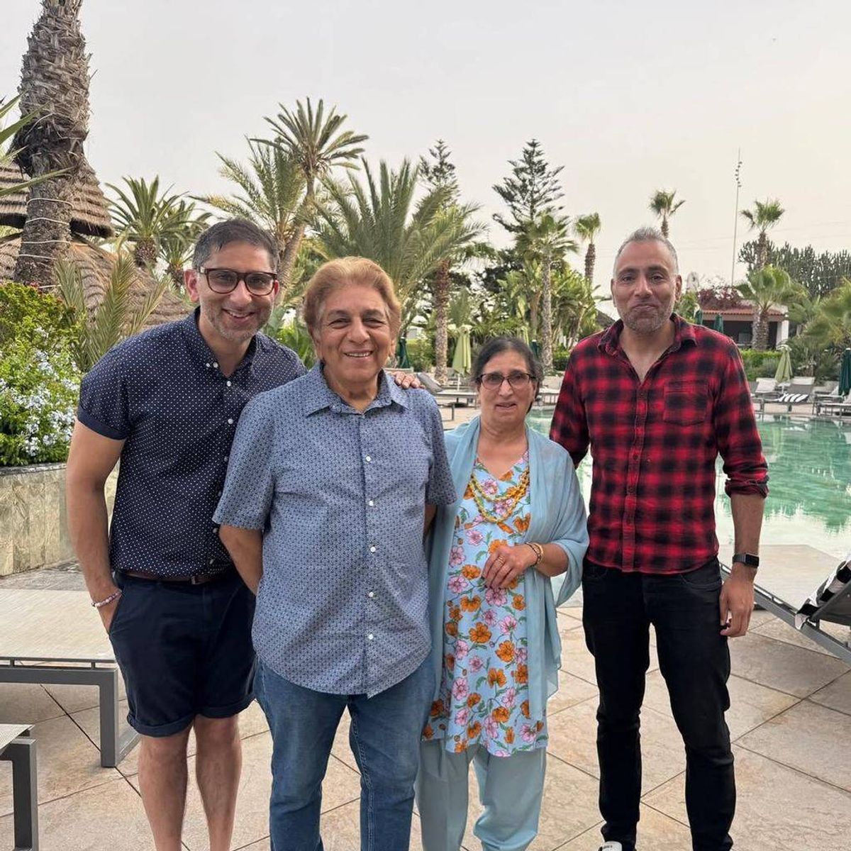 Four individuals, consisting of two men and two women, are standing together in front of a scenic backdrop featuring lush greenery and a pool.
