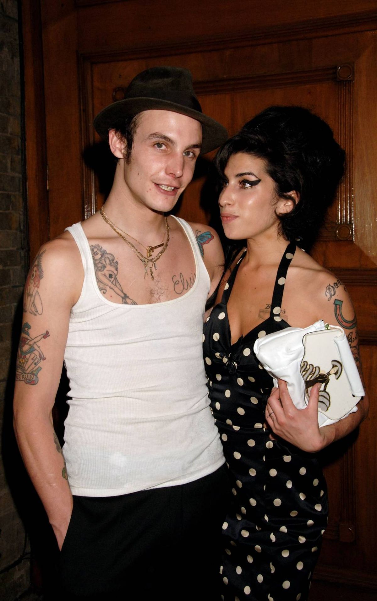 An individual with tattoos on their arms is standing next to another person with tattoos on their arms, both appearing to be posing for a photograph in an indoor setting.