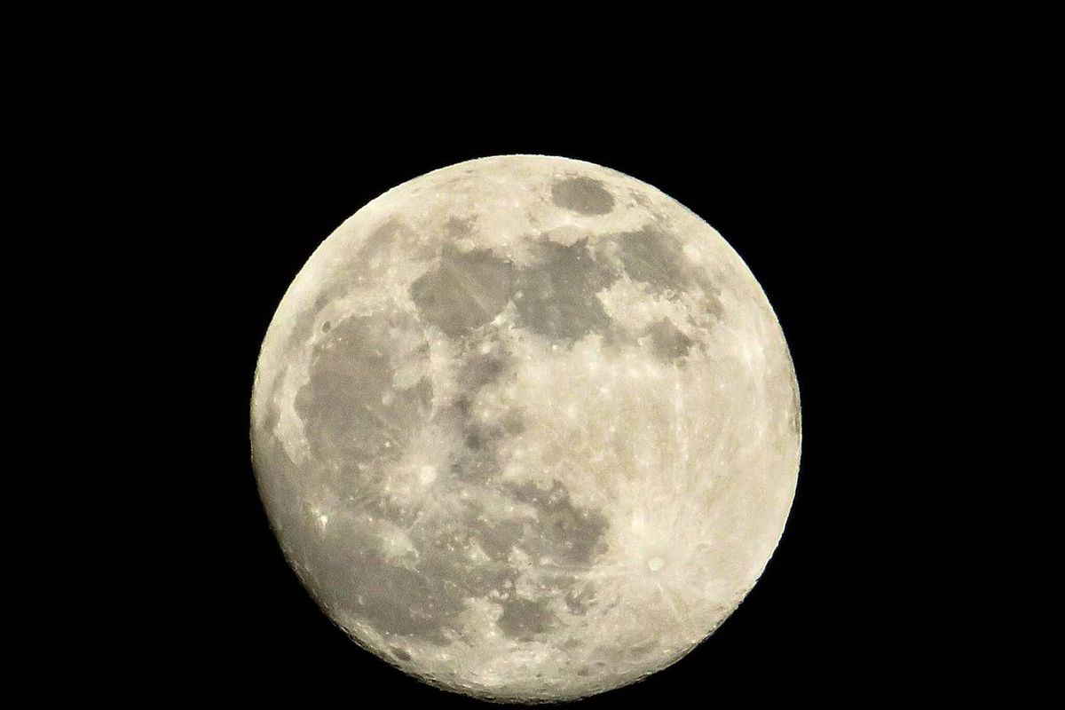 A full moon is prominently displayed against a dark night sky, showcasing its bright, luminous surface and distinct craters and shadowed areas.