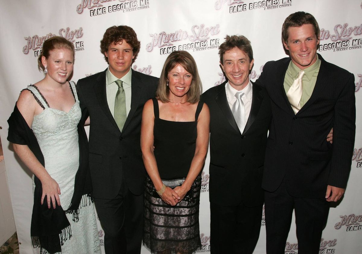 A group of individuals dressed in formal attire are standing together on a red carpet, likely at an awards ceremony. The setting suggests a celebratory and formal event, with a backdrop featuring text and logos.