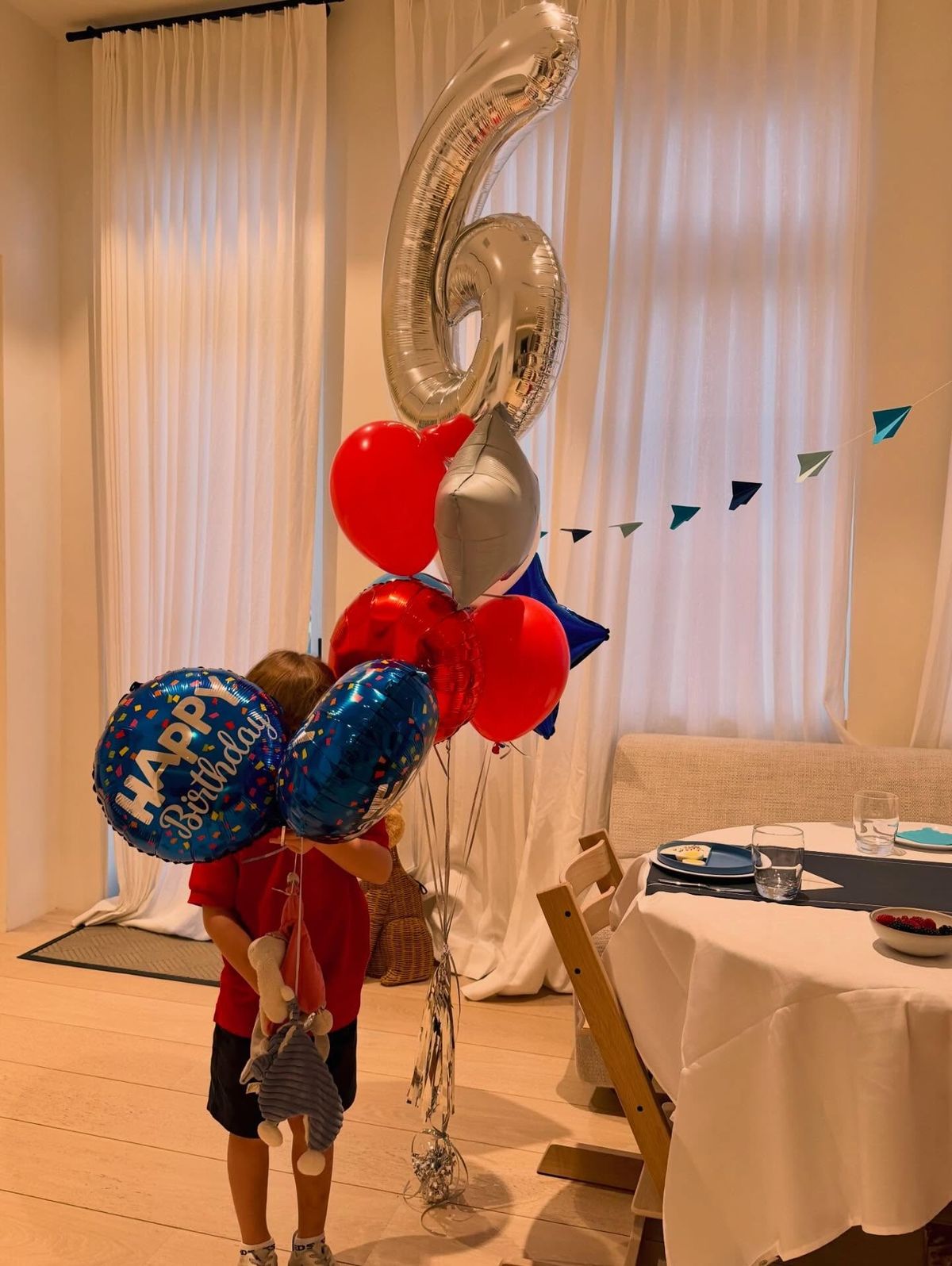 A young boy hides behind various birthday balloons