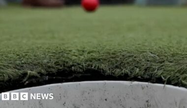A red gold ball travelling towards a hole on the course.