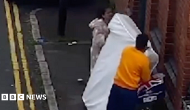 A man and a woman leaving a mattress against a brick wall