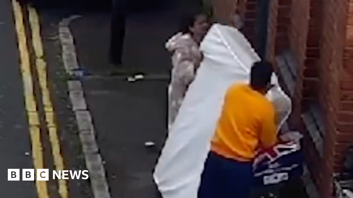 A man and a woman leaving a mattress against a brick wall