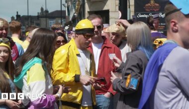 A group of people wearing fancy dress. One man dressed as Ali G is being asked for identification