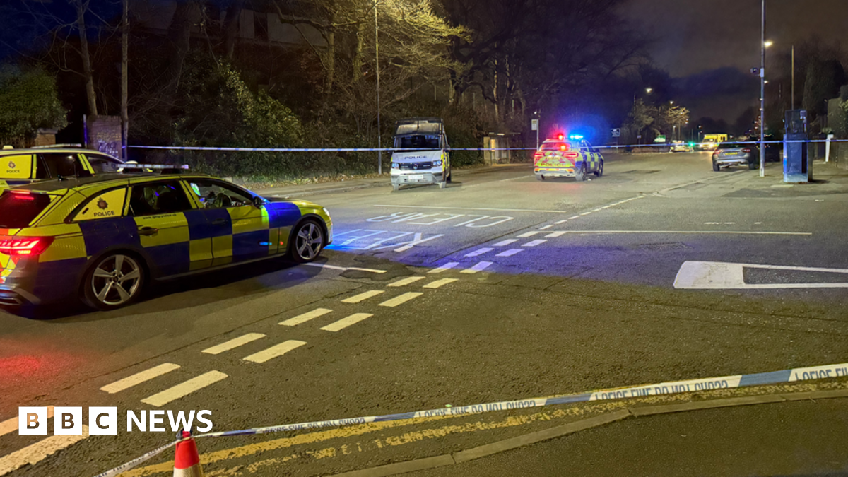 The scene of a fatal collision on a road at night, the area is cordoned off with police tape and there are several police cars at the scene with flashing lights.