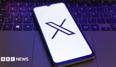 X logo displayed on a smartphone lying on a laptop keyboard