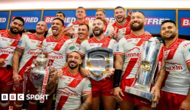 Hull KR players hold their three trophies and their winners rings in a posed photo in the dressing room after their Grand Final triumph over Wigan Warriors.