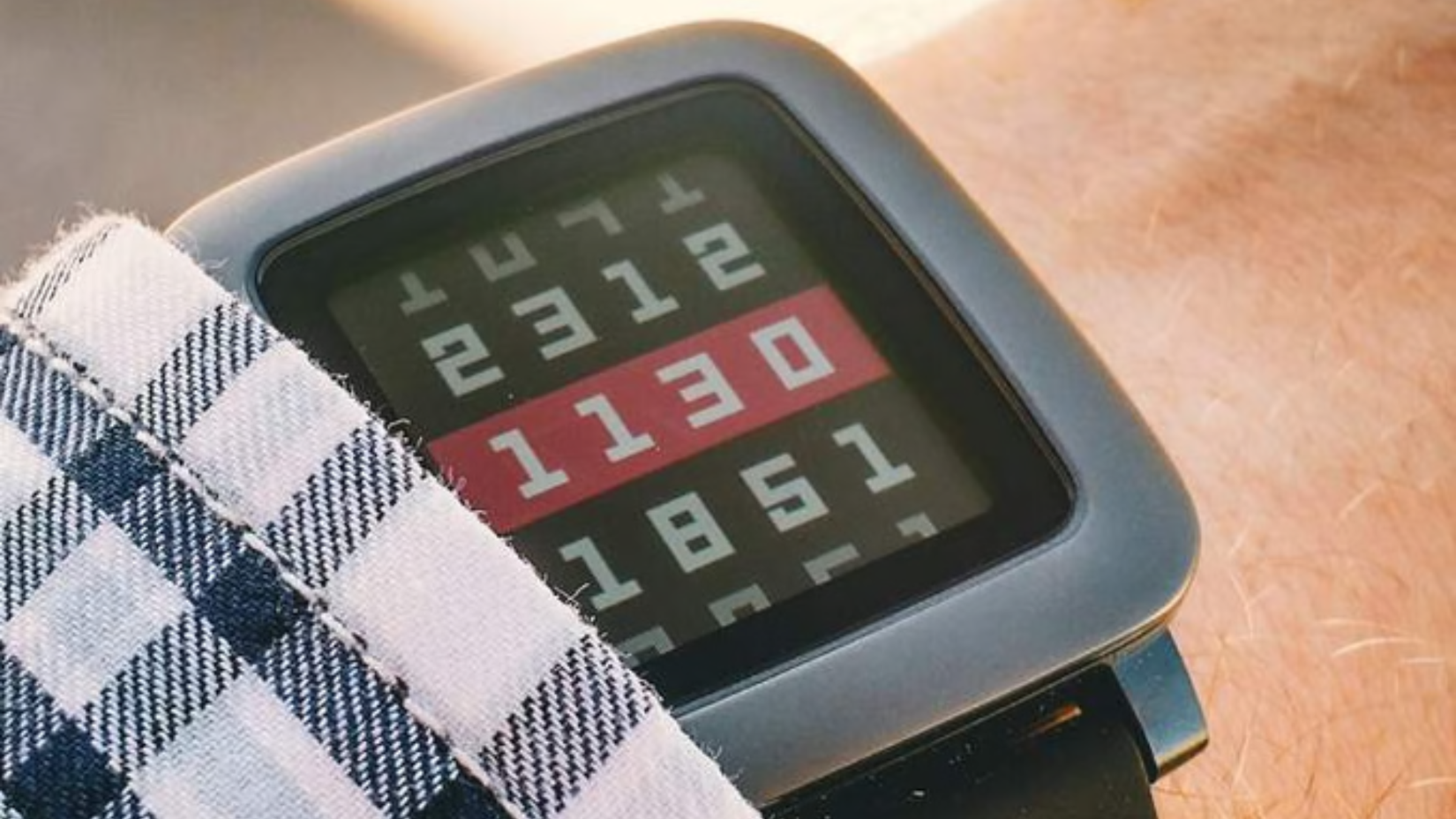 A Pebble Watch showing a series of digits ons someone's wrist 