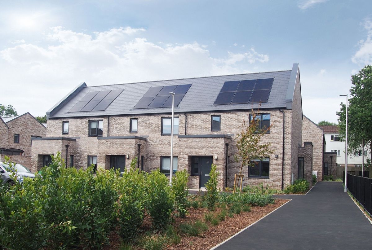 The rear of a terrace row of light brown brick houses with solar panels on the roof as part of the Iorwerth Jones development for Cardiff County Council