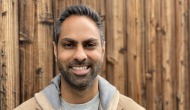 Ramit Sethi smiling with a wooden wall in the background.