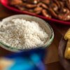 A bowl of white rice sits on a table next to a bowl of pasta spirals.