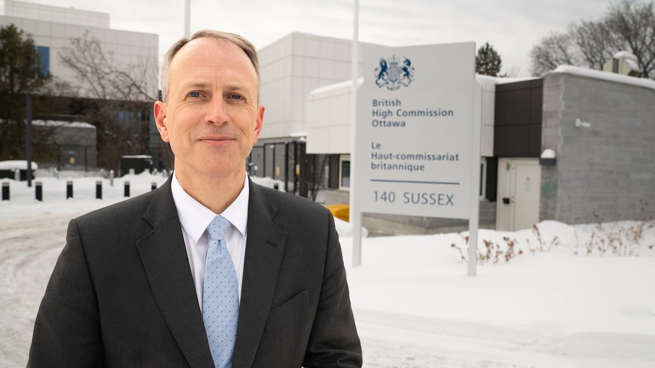 Man smiling in suit stands outside entrance to British High Commission in Ottawa