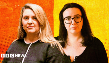 Sophie Hartley and Beth Cox pose together against a bold, stylized backdrop split into orange and yellow. Sophie on the left has long blonde hair and wears a dark buttoned top with white trim. Beth on the right has dark hair, glasses, and a black buttoned top. The background features a dotted, textured gradient that gives the image a modern, graphic look.