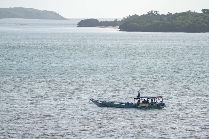 A man on a wooden boat in the ocean with one of the men waving.