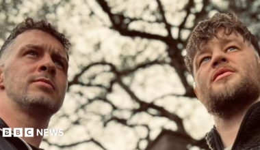 Two men in their mid twenties with beards look off into the distance.