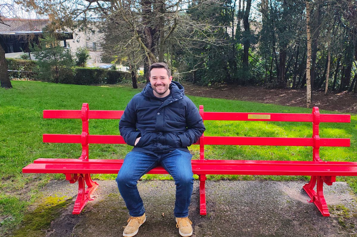A smiling man sitting on a park bench 