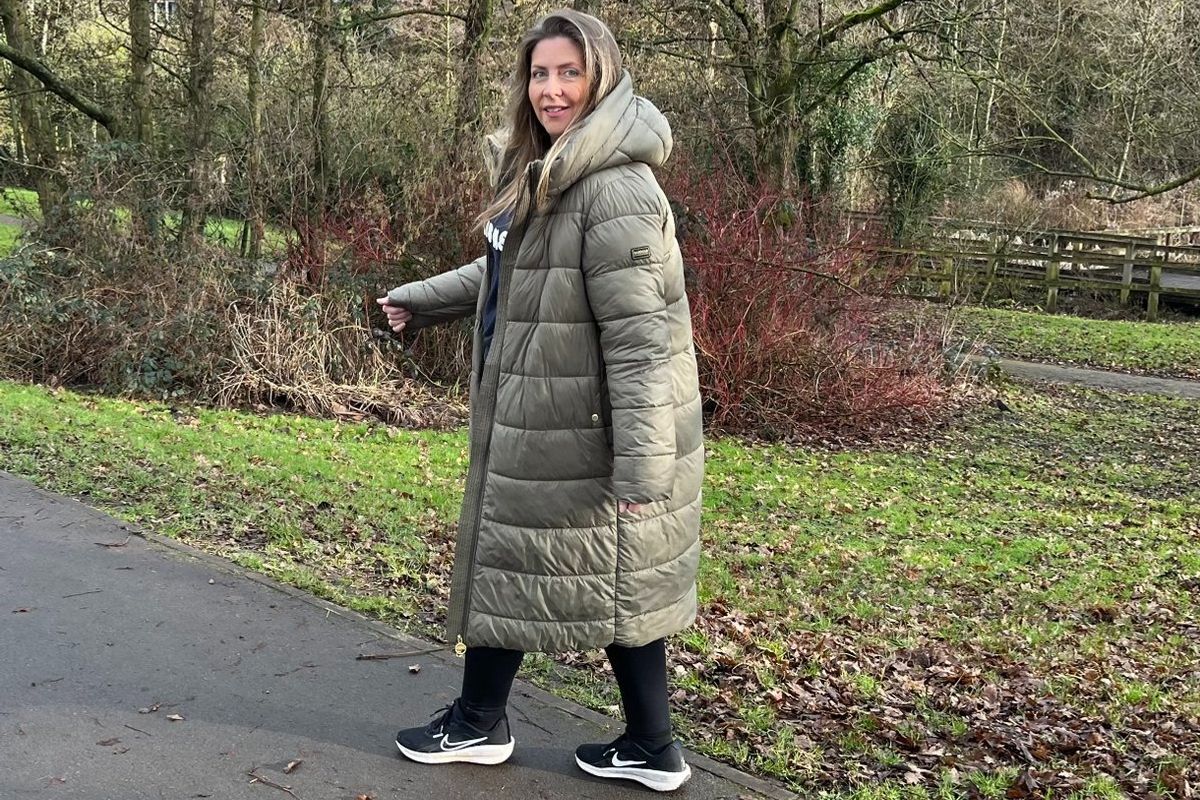 Woman in a long green jacket walking on a path in a park