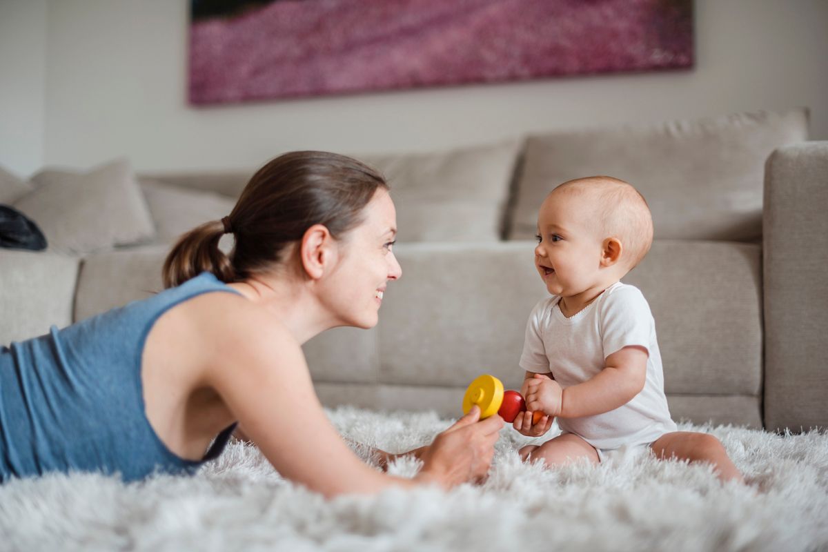 Happy baby girl with mother playing on carpet at home