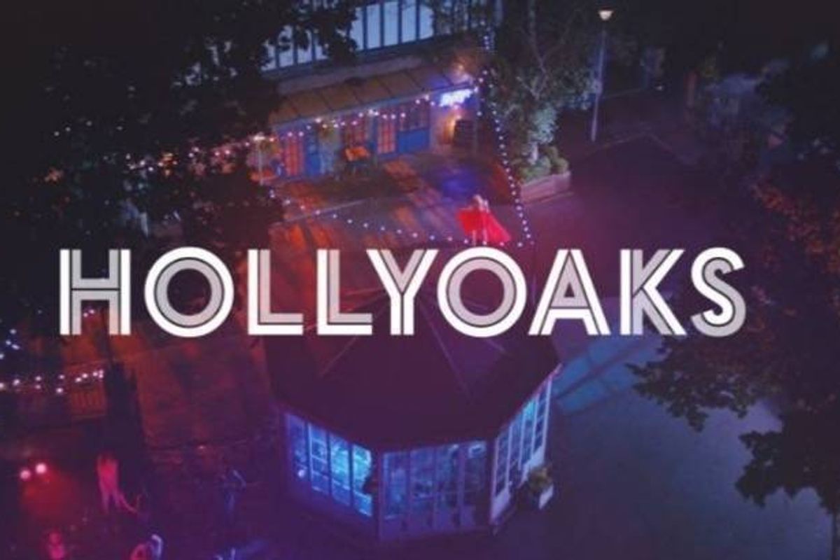 An aerial view of a nighttime cityscape is depicted, with the word "HOLLYOAKS" prominently displayed in white against a backdrop of vibrant, colorful lights and an urban skyline.