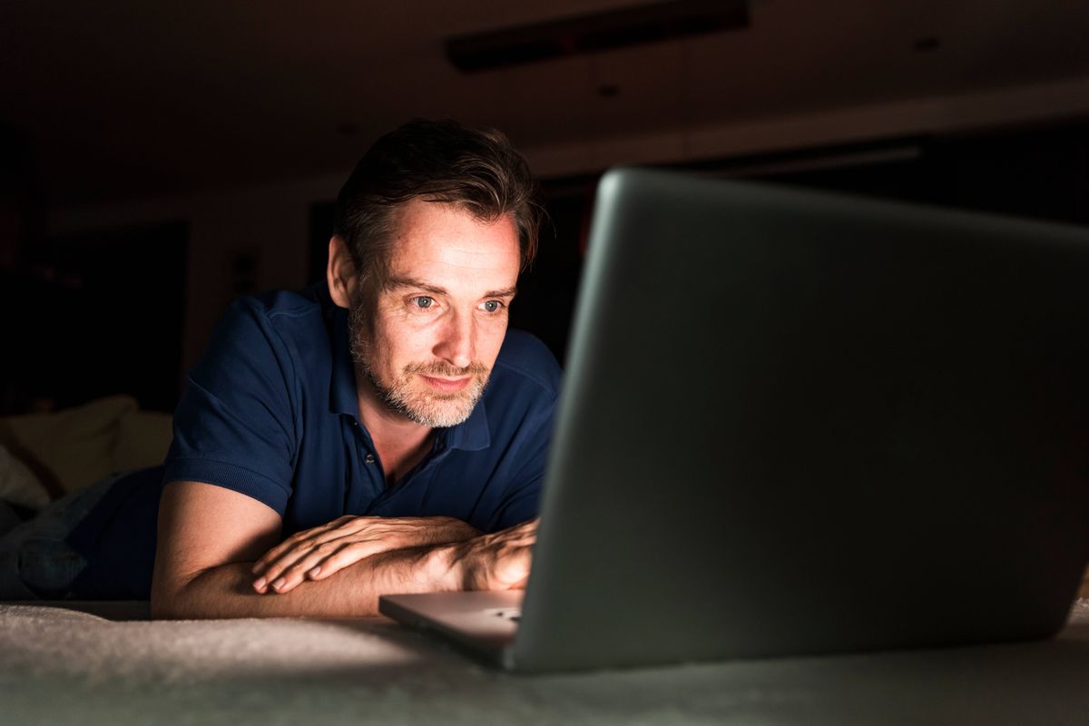 Portrait of man lying on couch at home looking at laptop