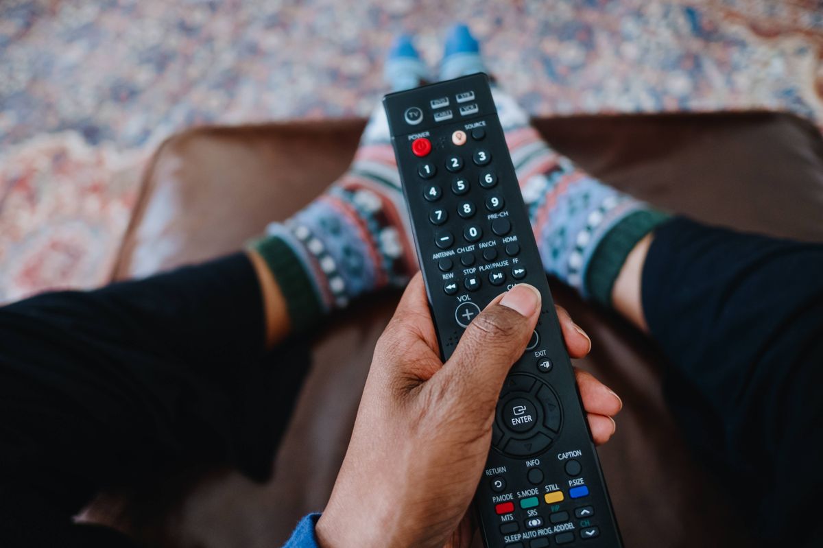 High angle view of unrecognizable black woman holding tv remote control while resting her feet on ottoman stool