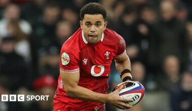 Ben Thomas holding the ball in both hands as he runs on the pitch