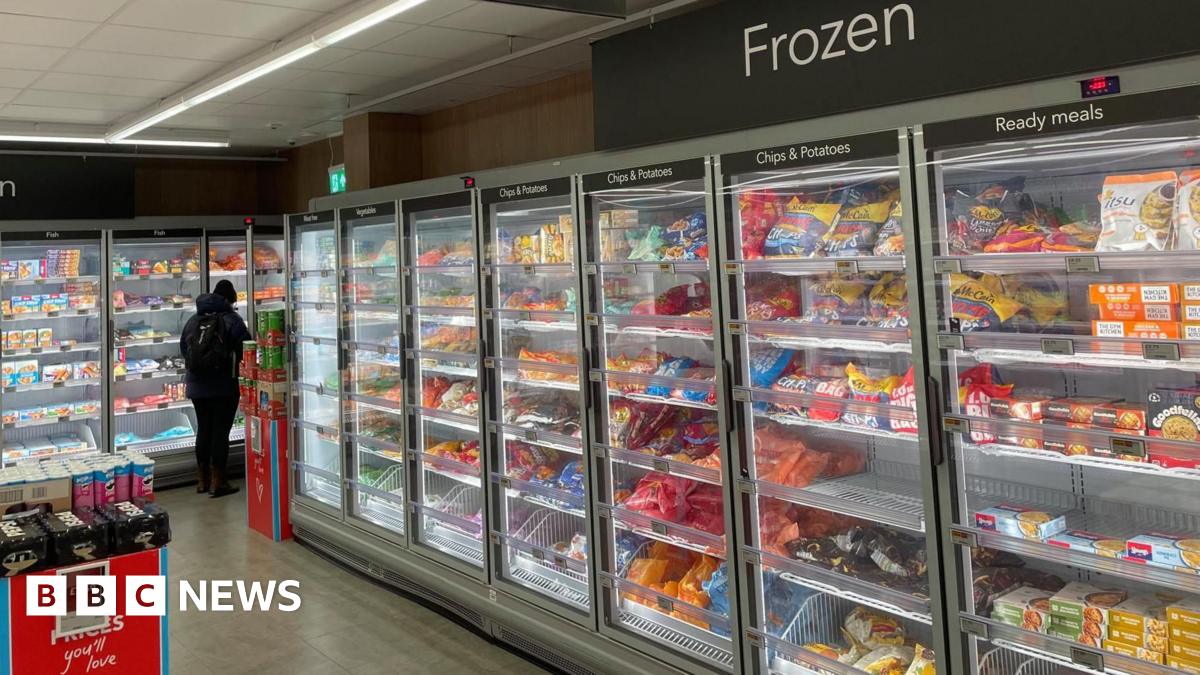 Rows of brightly coloured frozen food packets and bags stacked behind glass cabinets in a supermarket.