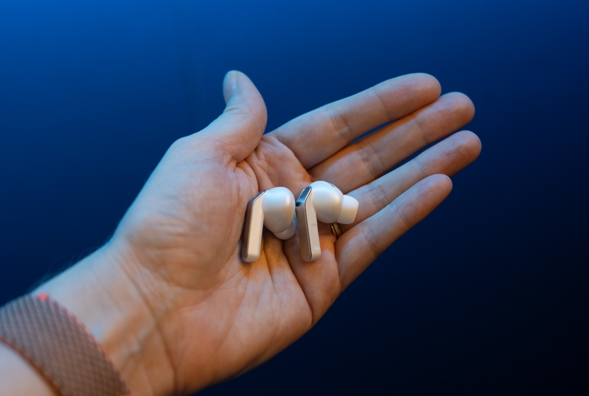 The Samsung Galaxy Buds 4 Pro in the palm of a hand with a blue background.
