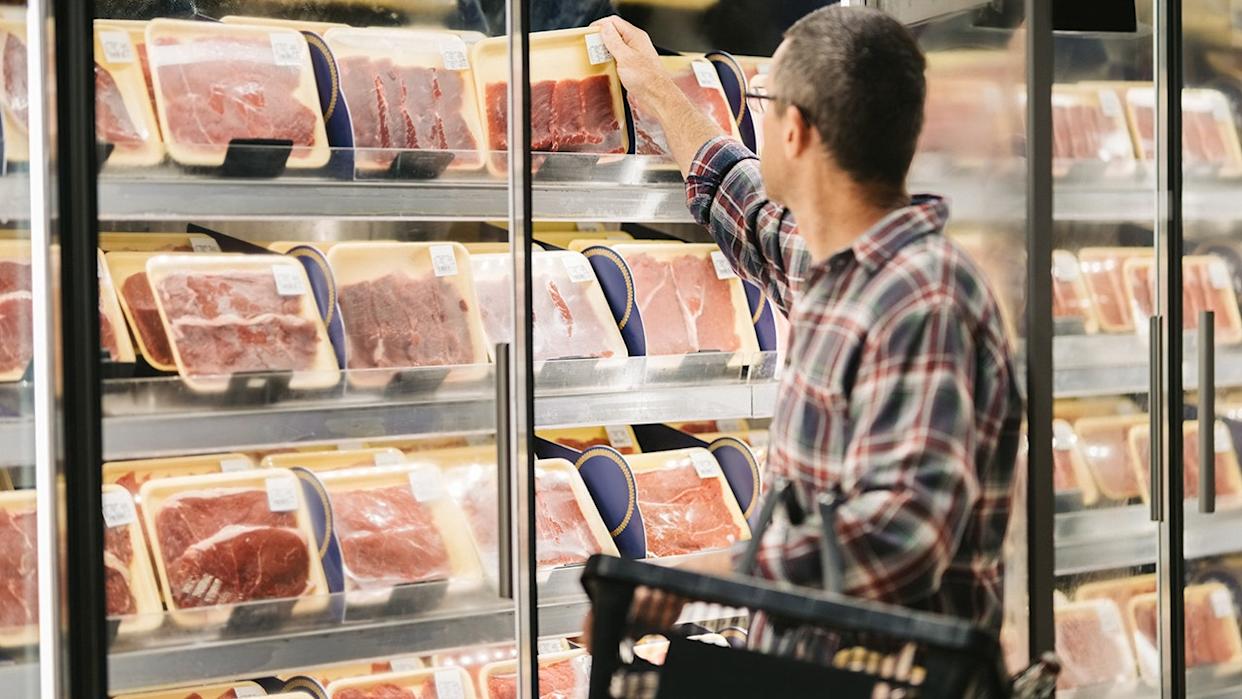 Male customer with a shopping basket taking meat from a fridge at local supermarket