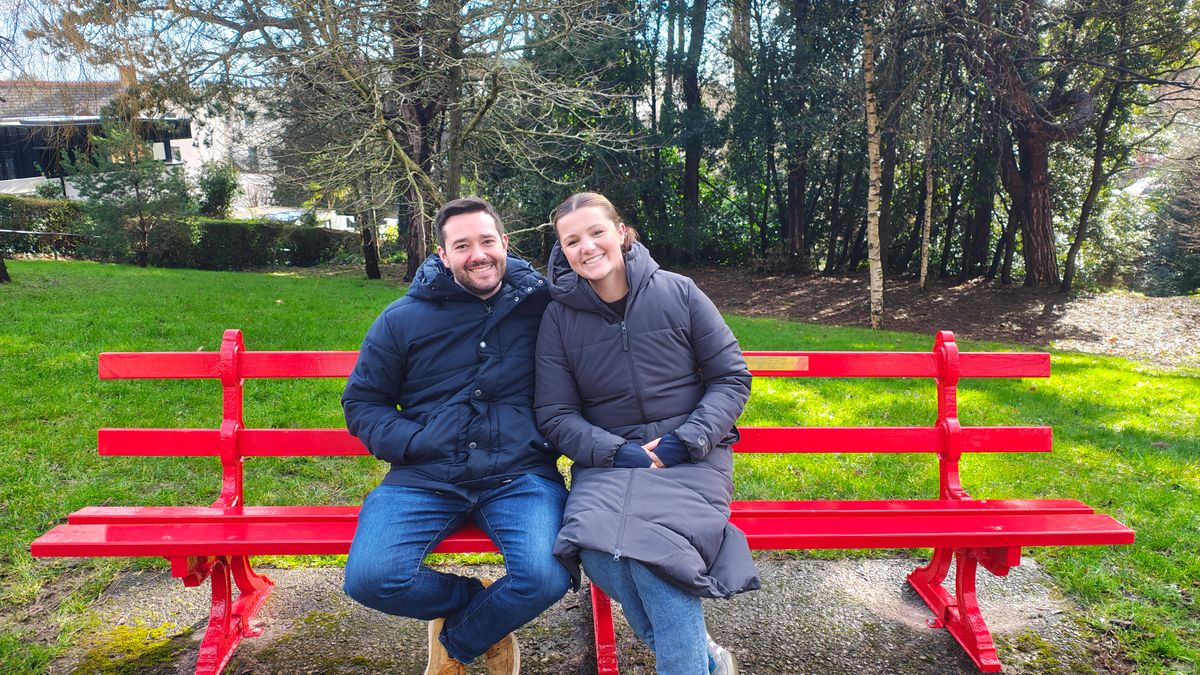 A young married couple sitting on a park bench smiling