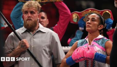 Jake Paul holding a flag pole and standing next to Amanda Serrano who is pushing her boxing gloves together