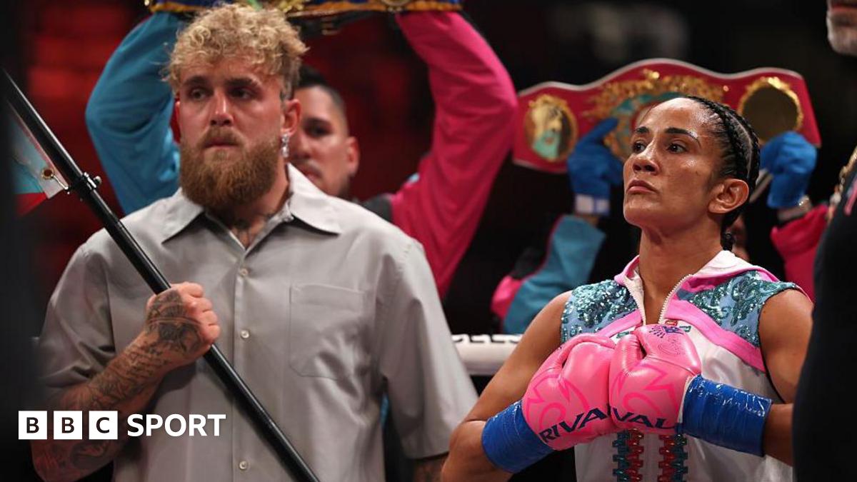 Jake Paul holding a flag pole and standing next to Amanda Serrano who is pushing her boxing gloves together