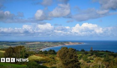 An ariel shot of the north of the Isle of Man, you can see the arching coastline, and there are houses scattered on the land amongst a lot of fields.