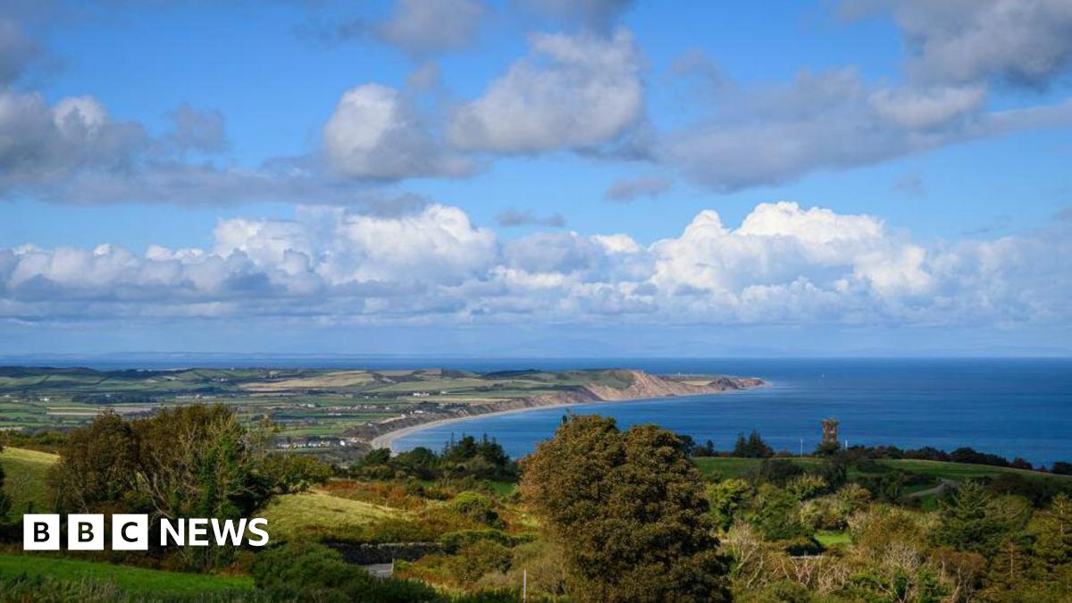 An ariel shot of the north of the Isle of Man, you can see the arching coastline, and there are houses scattered on the land amongst a lot of fields.