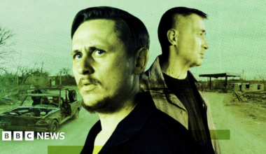 Ilya, wearing a blue denim jacket, looks out of the window in a warehouse in an undisclosed location.