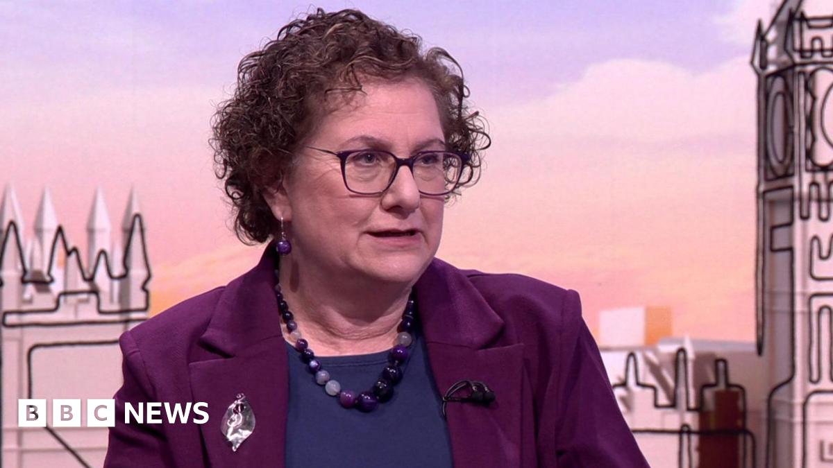 Hilary Cass on the Sunday With Laura Kuenssberg set. She has medium-length curly brown hair and is wearing a purple jacket, dark blue top and has a large purple bead necklace and purple bead earrings.